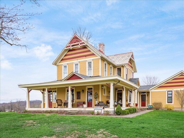 victorian-style house featuring a chimney, a front lawn, and covered porch