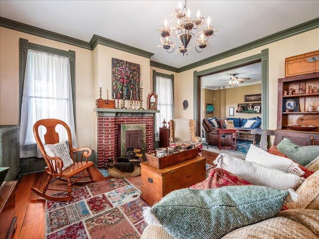 living area featuring a fireplace, hardwood / wood-style flooring, ornamental molding, and an inviting chandelier
