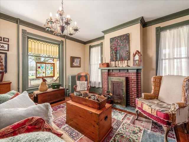 living area with a fireplace, wood finished floors, crown molding, and an inviting chandelier