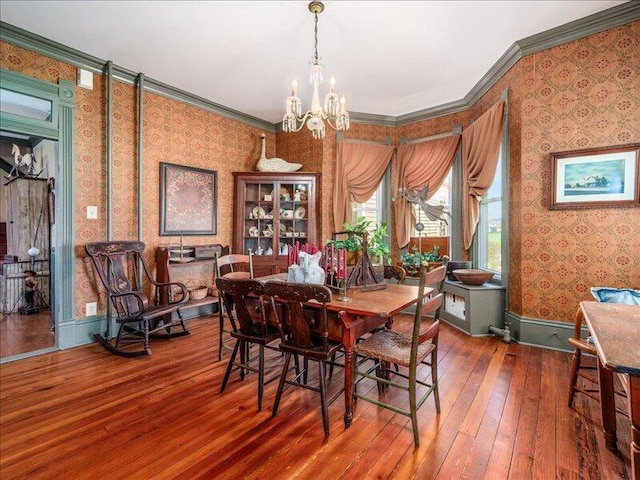 dining area with hardwood / wood-style floors, wallpapered walls, a chandelier, and ornamental molding