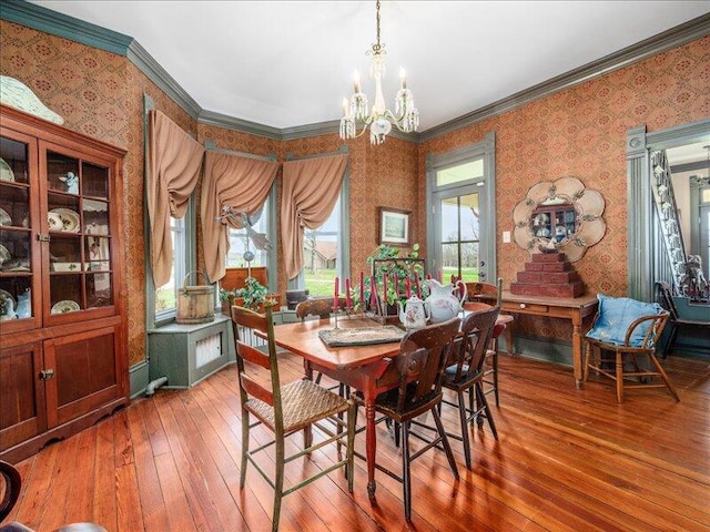dining space with an inviting chandelier, crown molding, hardwood / wood-style floors, and wallpapered walls