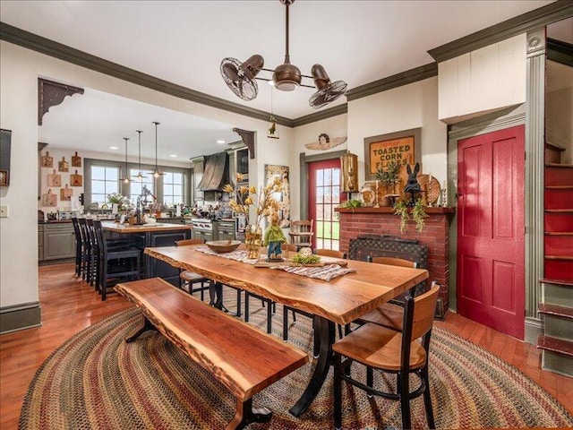 dining space featuring plenty of natural light, a brick fireplace, wood finished floors, and ornamental molding