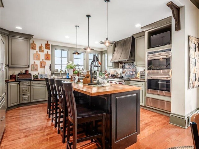 kitchen with a warming drawer, custom exhaust hood, gray cabinets, wooden counters, and double oven