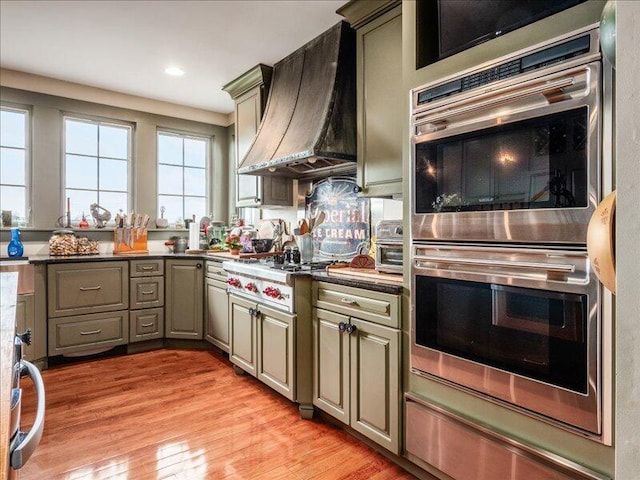 kitchen featuring gas cooktop, light wood finished floors, custom exhaust hood, recessed lighting, and stainless steel double oven