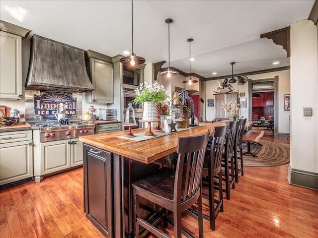 kitchen featuring a breakfast bar, light wood-style floors, stainless steel gas cooktop, wood counters, and custom exhaust hood