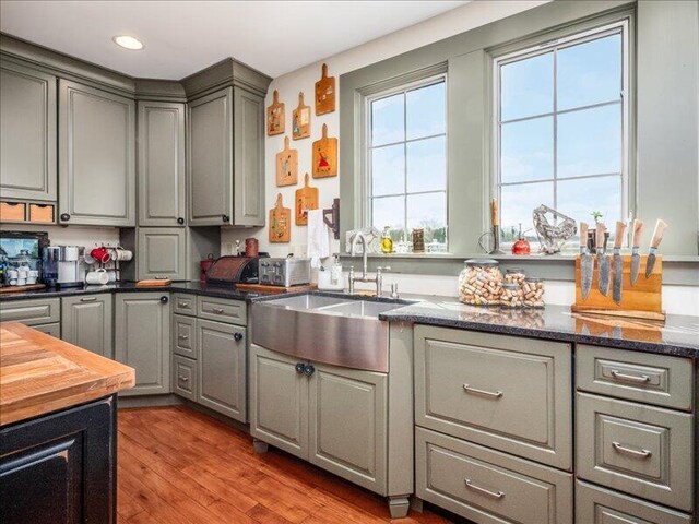 kitchen with a sink, dark stone counters, recessed lighting, wood finished floors, and gray cabinetry