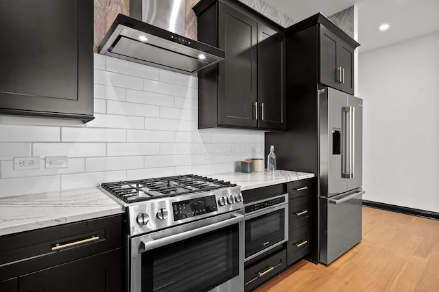 225 John H Mcconnell Blvd Unit 705, Columbus, OH 43215 - kitchen featuring light wood-style floors, wall chimney exhaust hood, dark cabinets, appliances with stainless steel finishes, and decorative backsplash