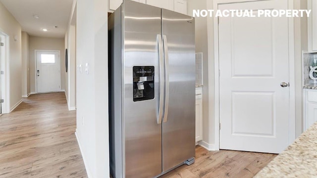 kitchen featuring stainless steel fridge with ice dispenser, light wood-type flooring, white cabinetry, light stone counters, and baseboards