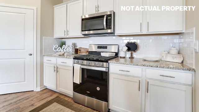 kitchen with light stone countertops, light wood-style flooring, white cabinetry, stainless steel appliances, and backsplash