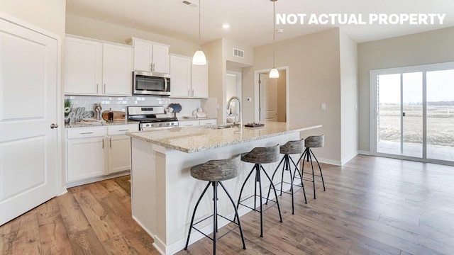 kitchen with light wood-style flooring, a kitchen island with sink, a sink, stainless steel appliances, and backsplash