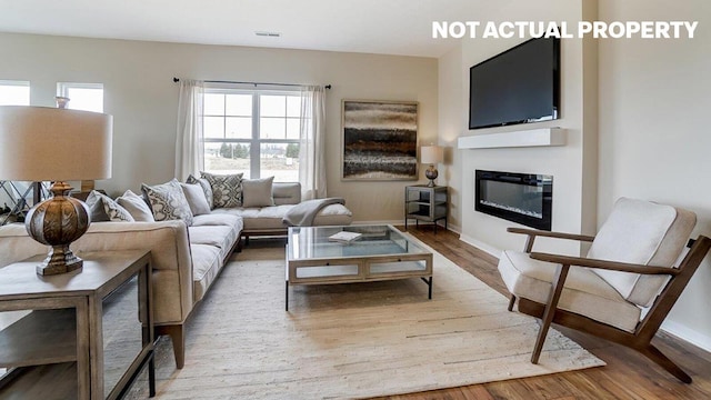 living area featuring visible vents, baseboards, a glass covered fireplace, and wood finished floors