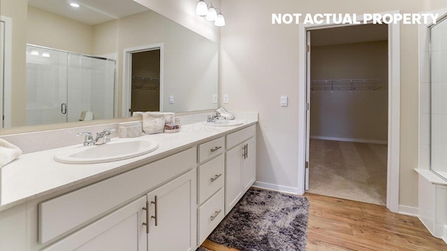 bathroom featuring double vanity, a shower stall, a walk in closet, a sink, and wood finished floors