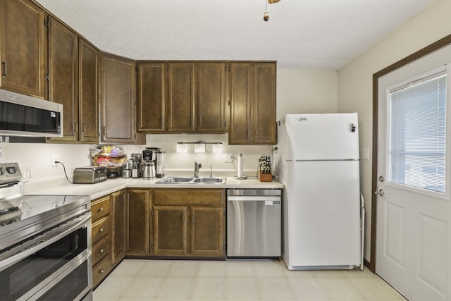 kitchen with dark brown cabinetry, light countertops, light floors, stainless steel appliances, and a sink