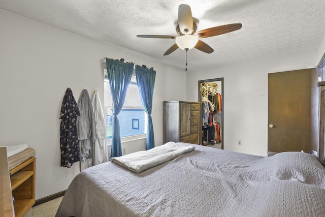 bedroom with ceiling fan, a textured ceiling, a closet, light carpet, and a walk in closet
