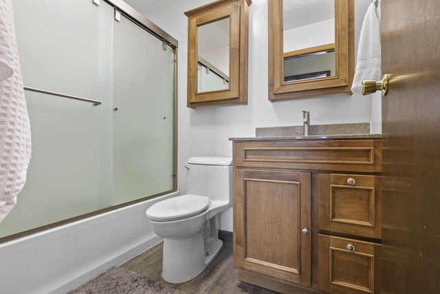 bathroom featuring combined bath / shower with glass door, vanity, a textured ceiling, toilet, and wood finished floors