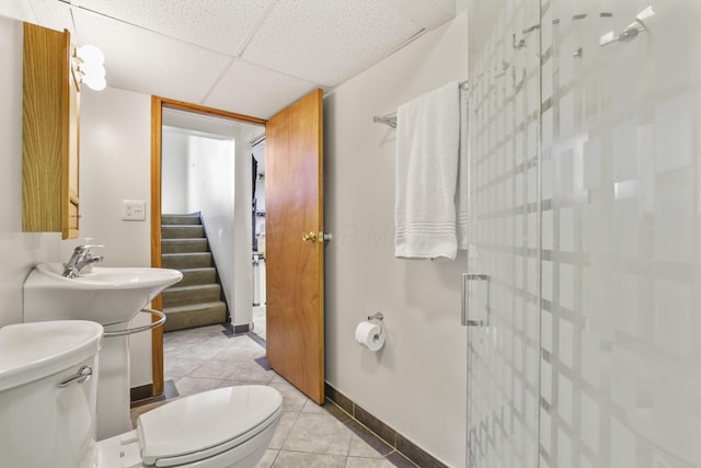 bathroom featuring baseboards, a stall shower, tile patterned flooring, toilet, and a drop ceiling