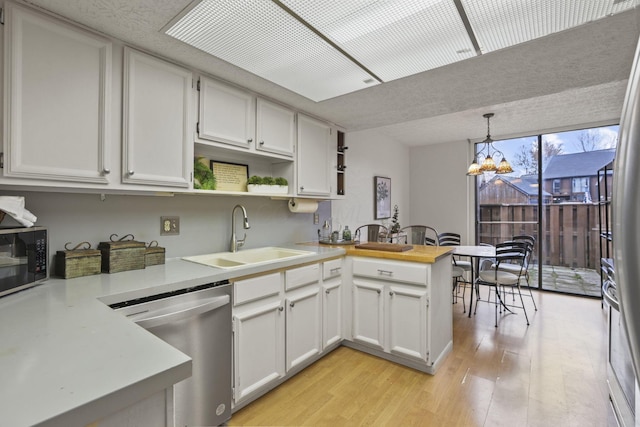 kitchen with light wood-type flooring, a peninsula, open shelves, stainless steel dishwasher, and a sink