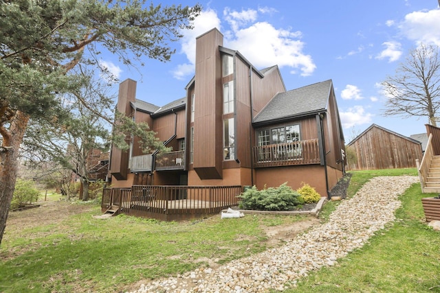 rear view of property with a shingled roof, a chimney, a wooden deck, and a yard