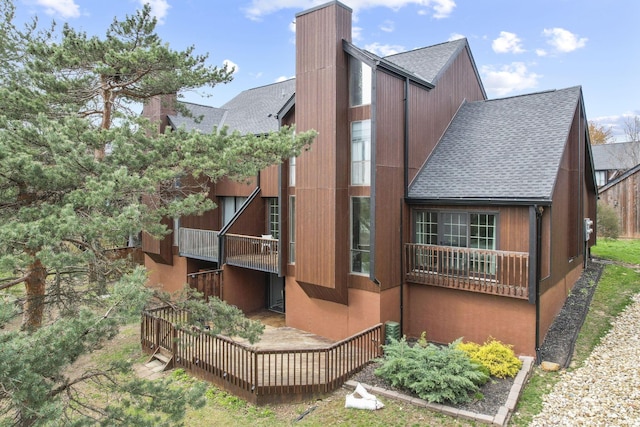 rear view of house featuring a chimney, a wooden deck, a balcony, and roof with shingles