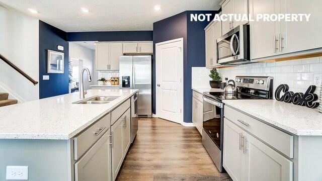 kitchen featuring light wood-type flooring, a kitchen island with sink, a sink, stainless steel appliances, and backsplash