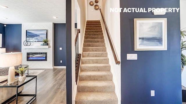 staircase featuring a fireplace, baseboards, wood finished floors, and a textured ceiling
