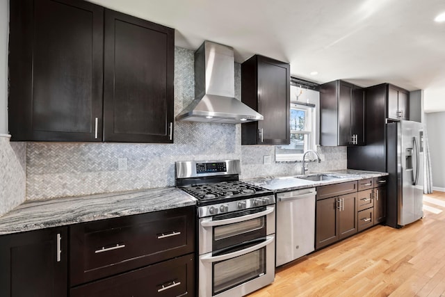 2209 Fishinger Rd, Columbus, OH 43221 - kitchen featuring wall chimney range hood, appliances with stainless steel finishes, light wood-type flooring, a sink, and light stone counters