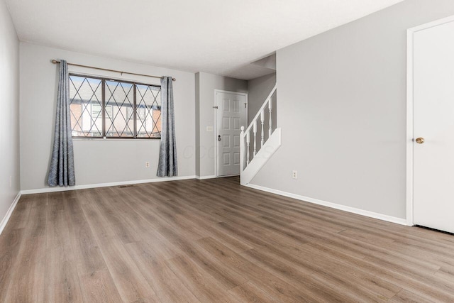 unfurnished living room with visible vents, baseboards, wood finished floors, and stairway