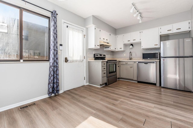 kitchen featuring under cabinet range hood, stainless steel appliances, visible vents, a sink, and light wood-style flooring