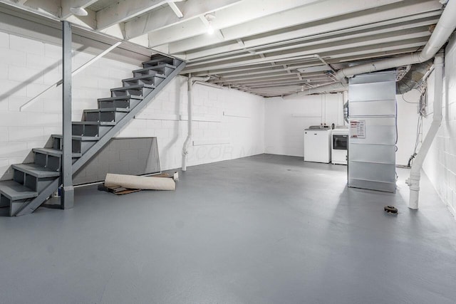 unfinished basement with concrete block wall, stairs, and washer and clothes dryer