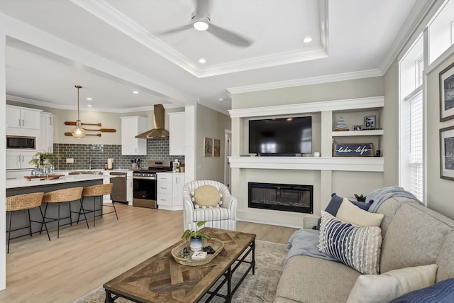 living room featuring a glass covered fireplace, light wood-style flooring, ornamental molding, and ceiling fan