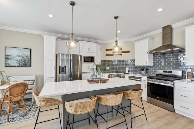 kitchen with crown molding, appliances with stainless steel finishes, wall chimney exhaust hood, and a kitchen breakfast bar