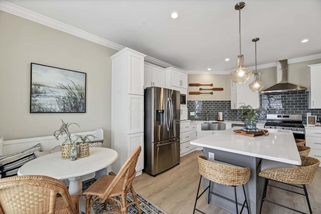 kitchen featuring wall chimney exhaust hood, white cabinets, appliances with stainless steel finishes, light countertops, and a sink