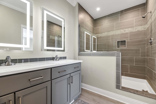 bathroom with a sink, a tile shower, double vanity, and wood finished floors