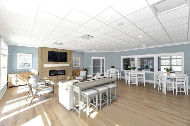living area with a paneled ceiling, crown molding, recessed lighting, a large fireplace, and light wood-style flooring