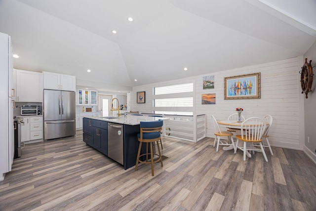 kitchen featuring lofted ceiling, white cabinetry, a sink, appliances with stainless steel finishes, and a center island with sink