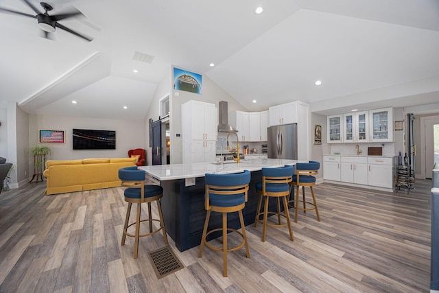 kitchen with light wood-type flooring, wall chimney exhaust hood, white cabinetry, freestanding refrigerator, and lofted ceiling