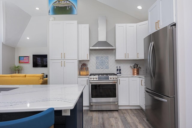 kitchen with wall chimney exhaust hood, lofted ceiling, white cabinetry, and stainless steel appliances