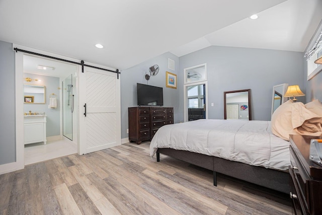 bedroom with lofted ceiling, a barn door, visible vents, baseboards, and wood finished floors