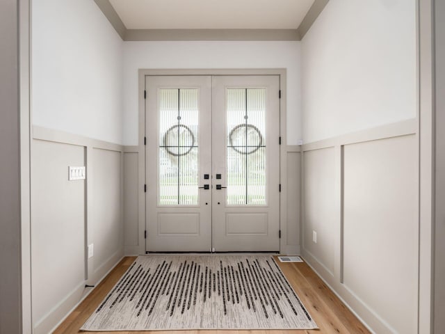 doorway to outside with french doors, a wainscoted wall, a decorative wall, and light wood-type flooring