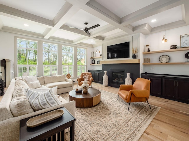 living area featuring a healthy amount of sunlight, beamed ceiling, a ceiling fan, and a fireplace with flush hearth