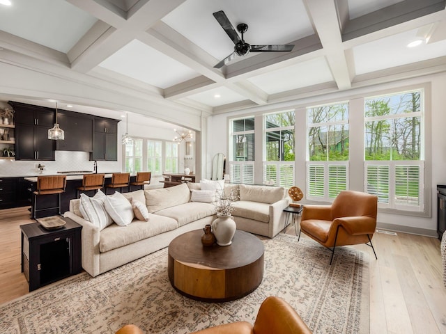living room with light wood-type flooring, beam ceiling, ceiling fan with notable chandelier, coffered ceiling, and recessed lighting