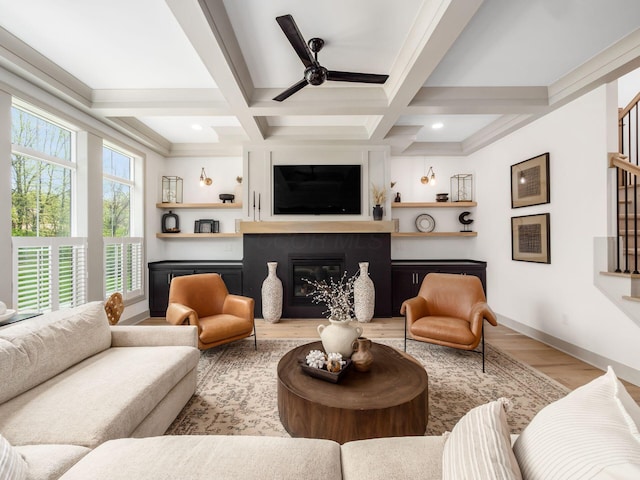 living area with ceiling fan, a glass covered fireplace, wood finished floors, beamed ceiling, and coffered ceiling