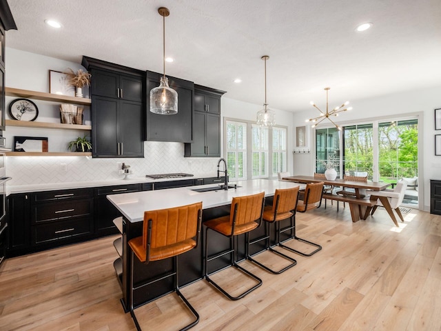 kitchen with a sink, light countertops, open shelves, and dark cabinets