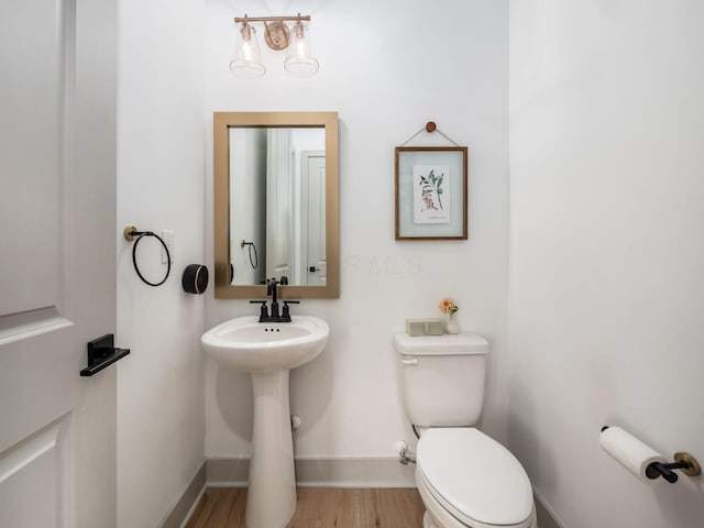 half bathroom with toilet, baseboards, a sink, and wood finished floors