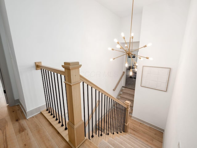 staircase with baseboards, wood finished floors, and a notable chandelier