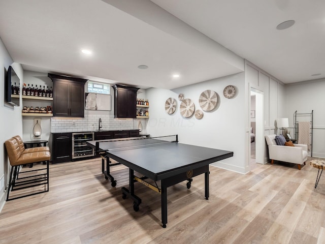 rec room with wine cooler, light wood-style floors, indoor wet bar, and a sink