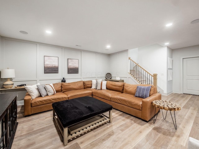 living room with recessed lighting, light wood finished floors, a decorative wall, and stairway