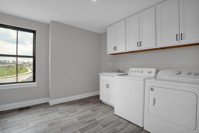 laundry area with light wood finished floors, plenty of natural light, cabinet space, and washer and clothes dryer