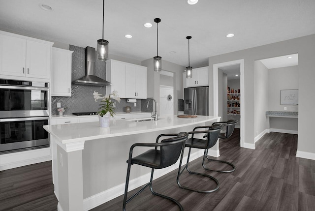 kitchen with a sink, wall chimney exhaust hood, stainless steel appliances, light countertops, and decorative backsplash