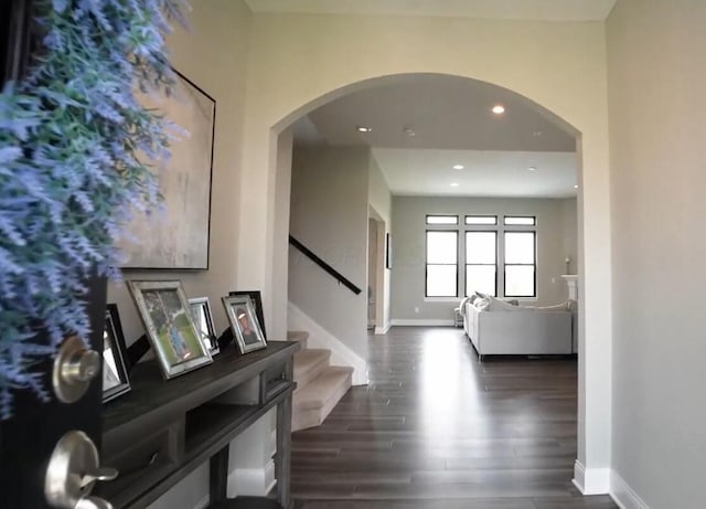 hallway with baseboards, stairway, arched walkways, and dark wood-type flooring